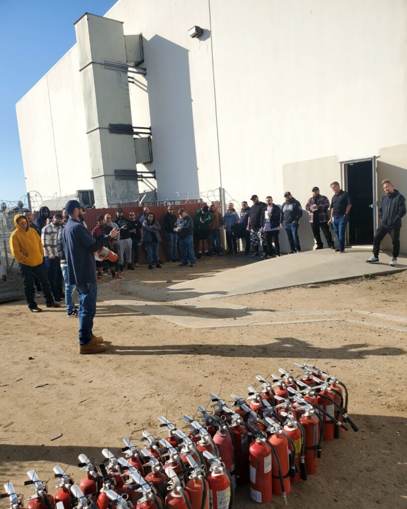 Male talking with a gathered crowd to discuss fire extinguisher safety and use.